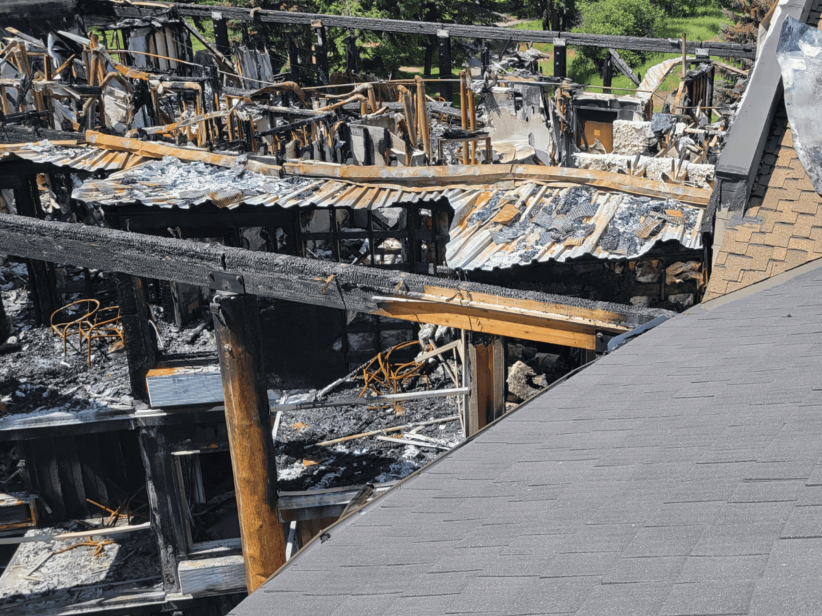 Fire-damaged lodge showing extensive structural destruction beside an intact Enviroshake roof section.