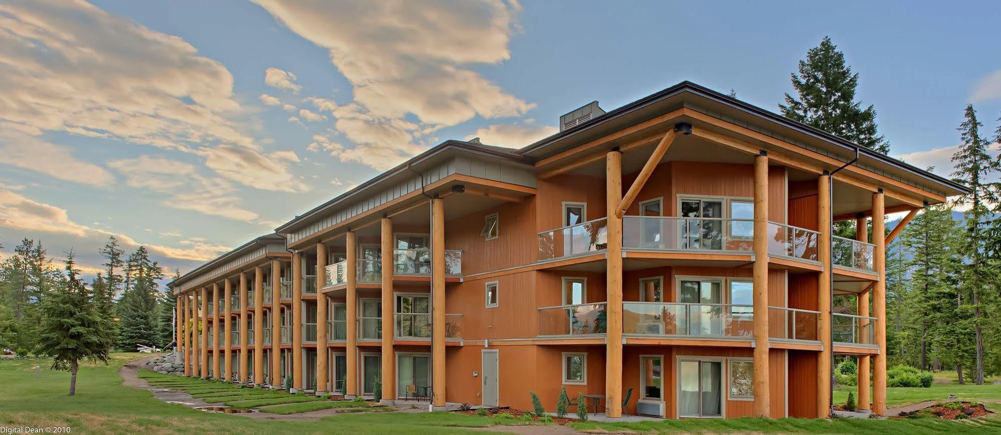 Large mountain lodge with timber columns, balconies and a low-slope roof surrounded by evergreen trees.