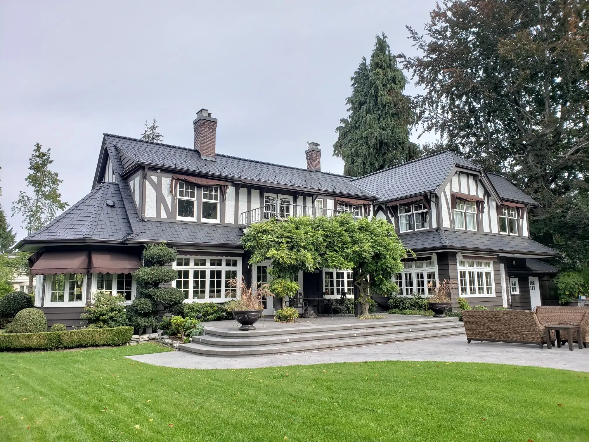 Enviroshake composite shake roofing on a Tudor-style home with dark roofing, landscaped gardens and a backyard patio.