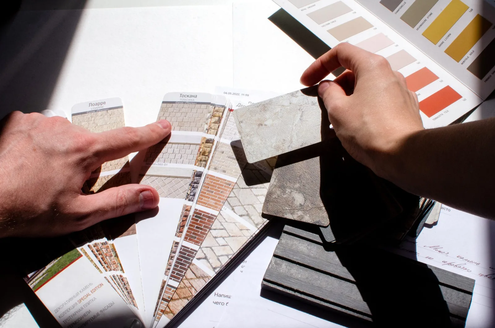 Hands comparing paint and material sample swatches with brick and stone catalogs