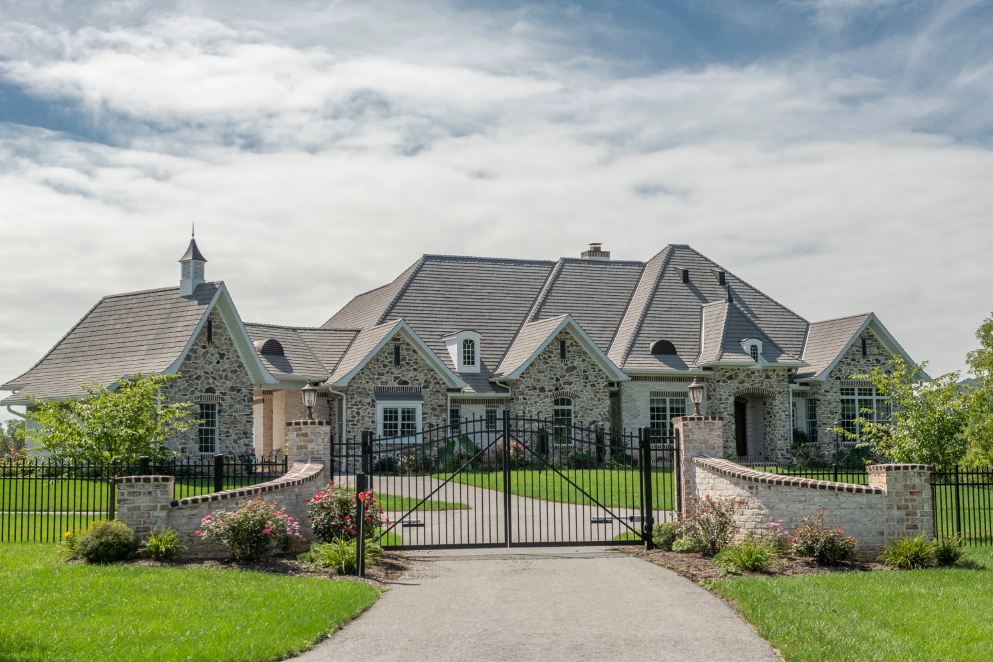 Stone French country home with an Enviroshake Aged Cedar roof behind a gated drive