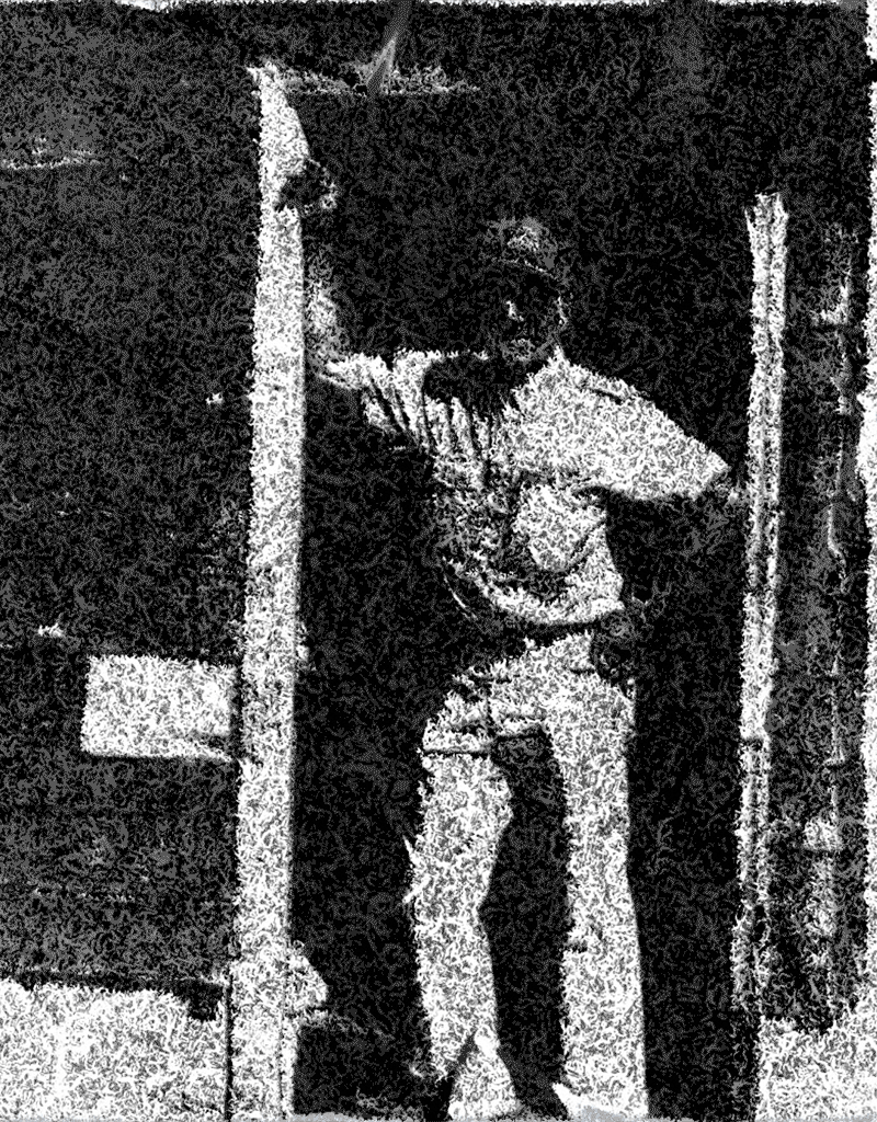 Man standing casually in a doorway, wearing light-colored pants and a shirt.