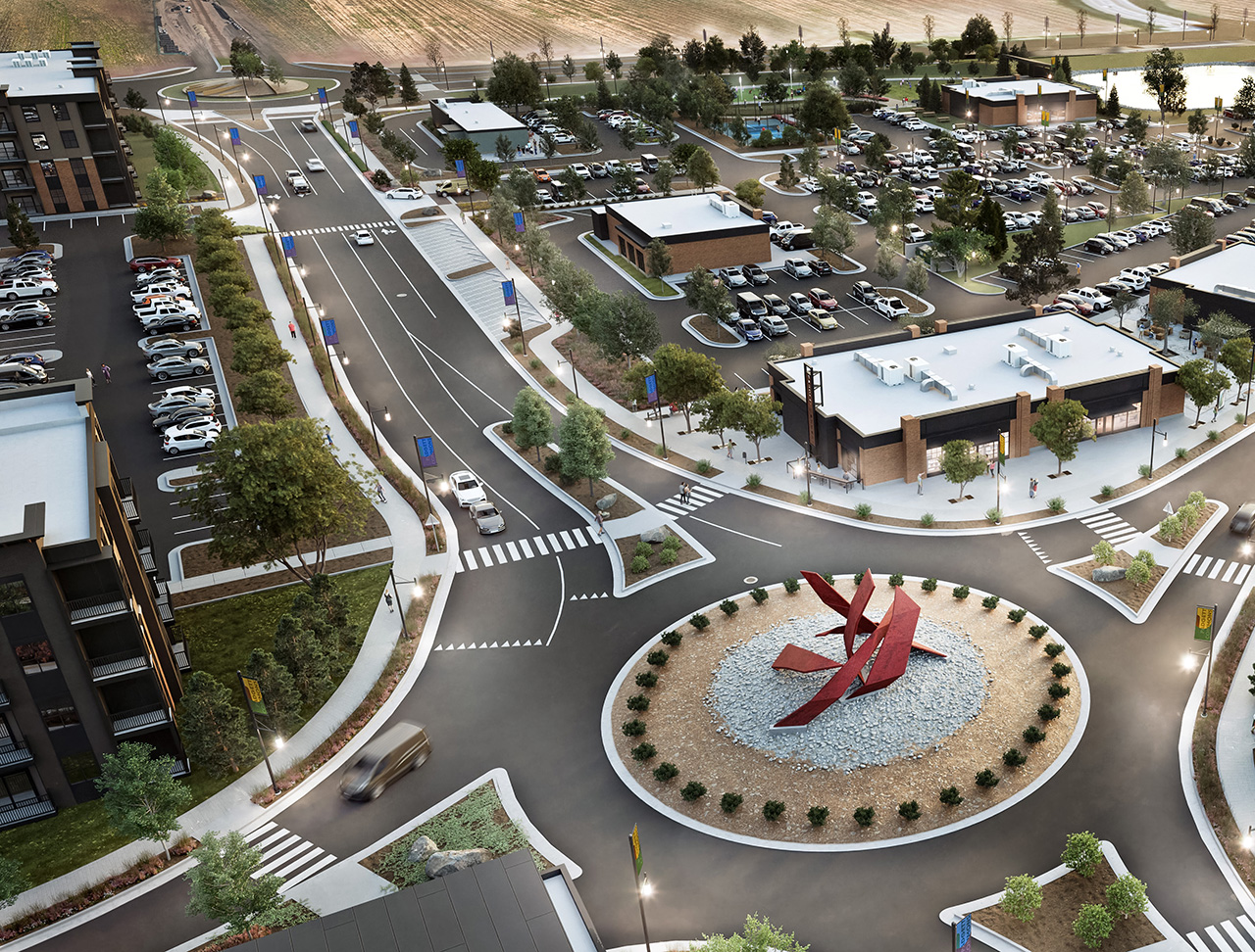 Aerial view of a roundabout with red abstract sculpture surrounded by parking lots and buildings.