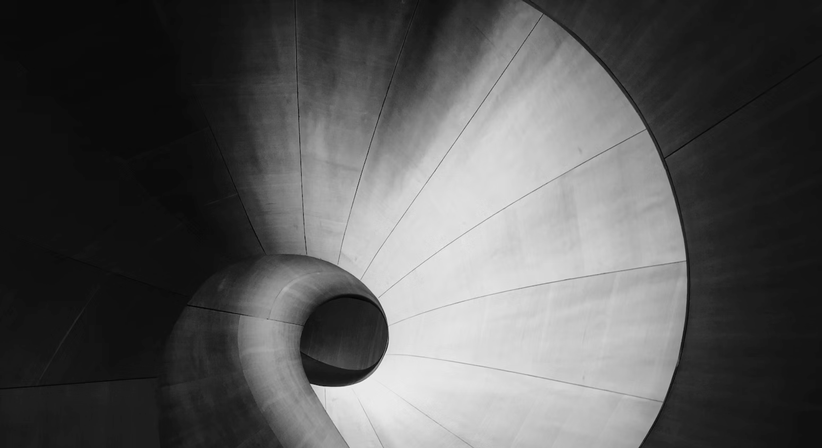 Black and white photo of a spiral concrete staircase viewed from above looking down.