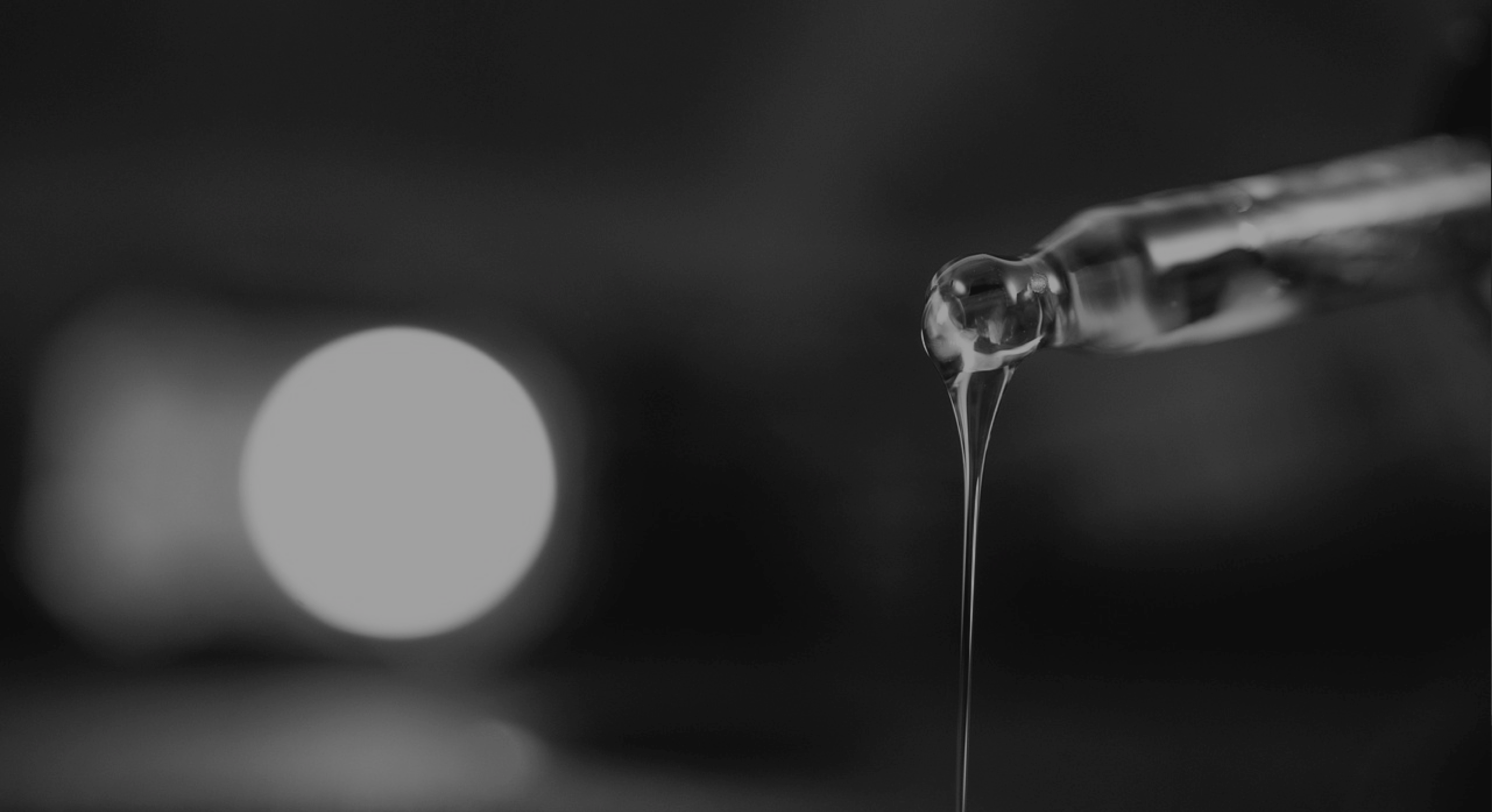 Close-up of a dropper releasing liquid in a blurred dark background.