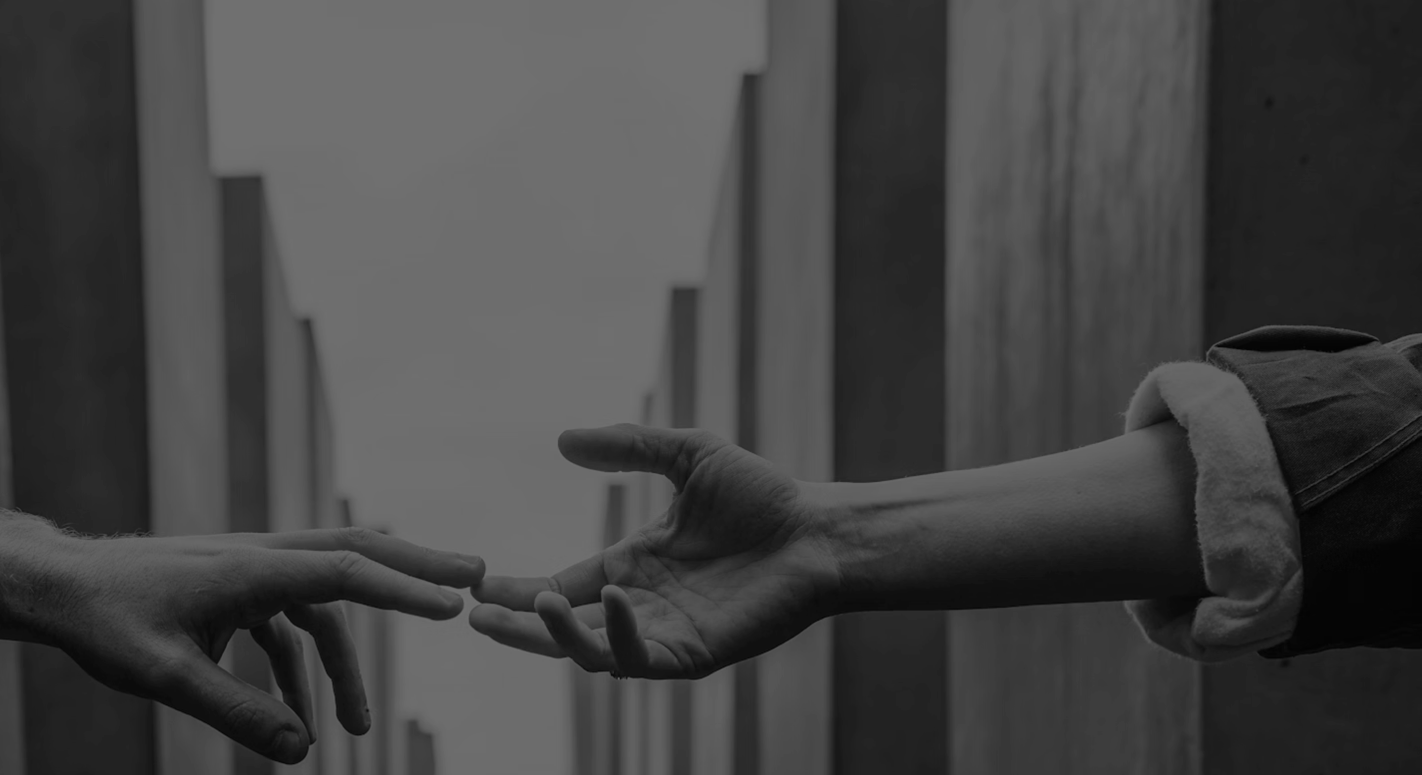 Two hands reaching toward each other with fingers almost touching in a grayscale photo.