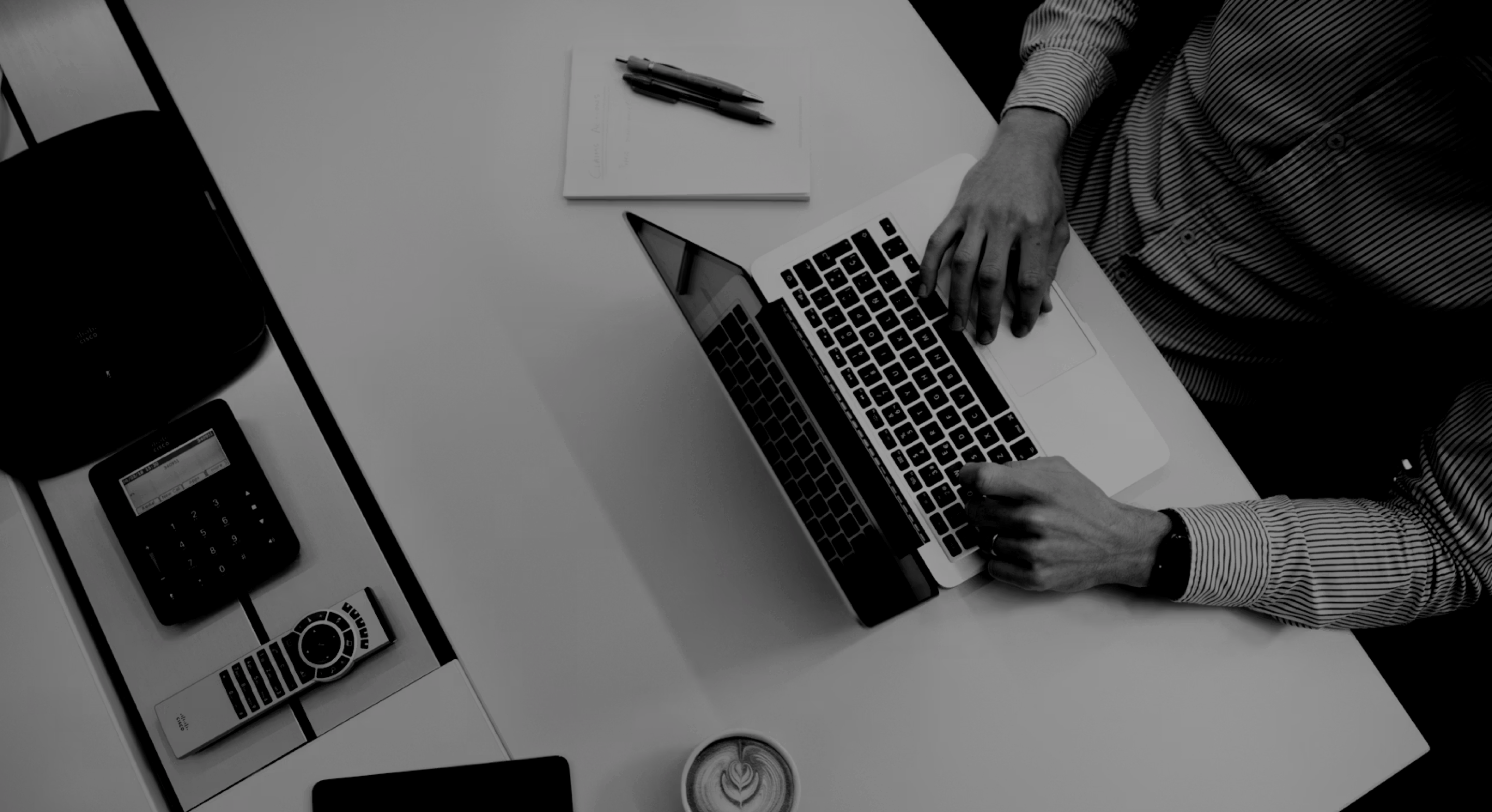 Top view of a person typing on a laptop beside a coffee cup and office phone on a white desk.