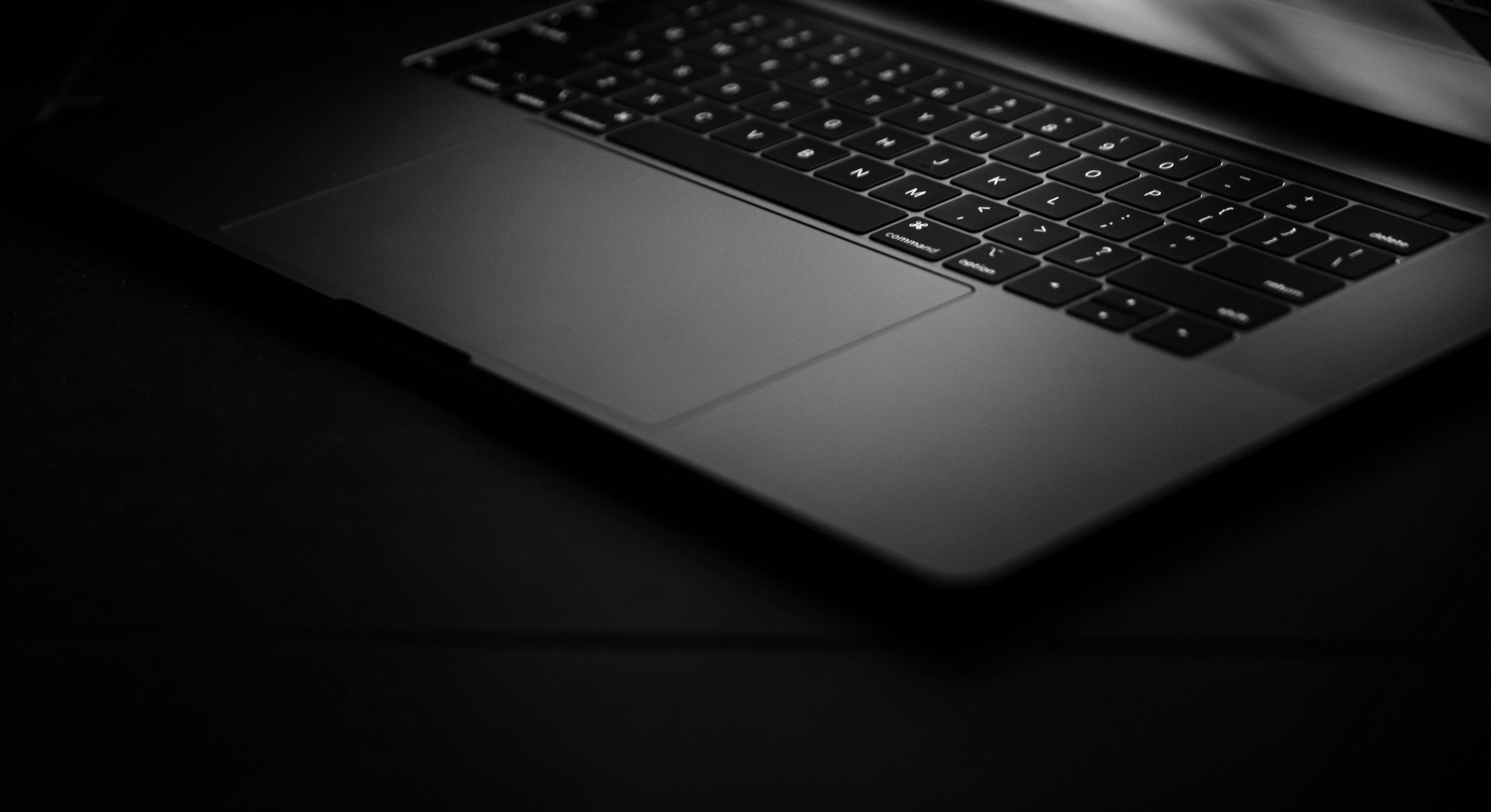 Close-up of a laptop keyboard and trackpad in low light with a dark background.