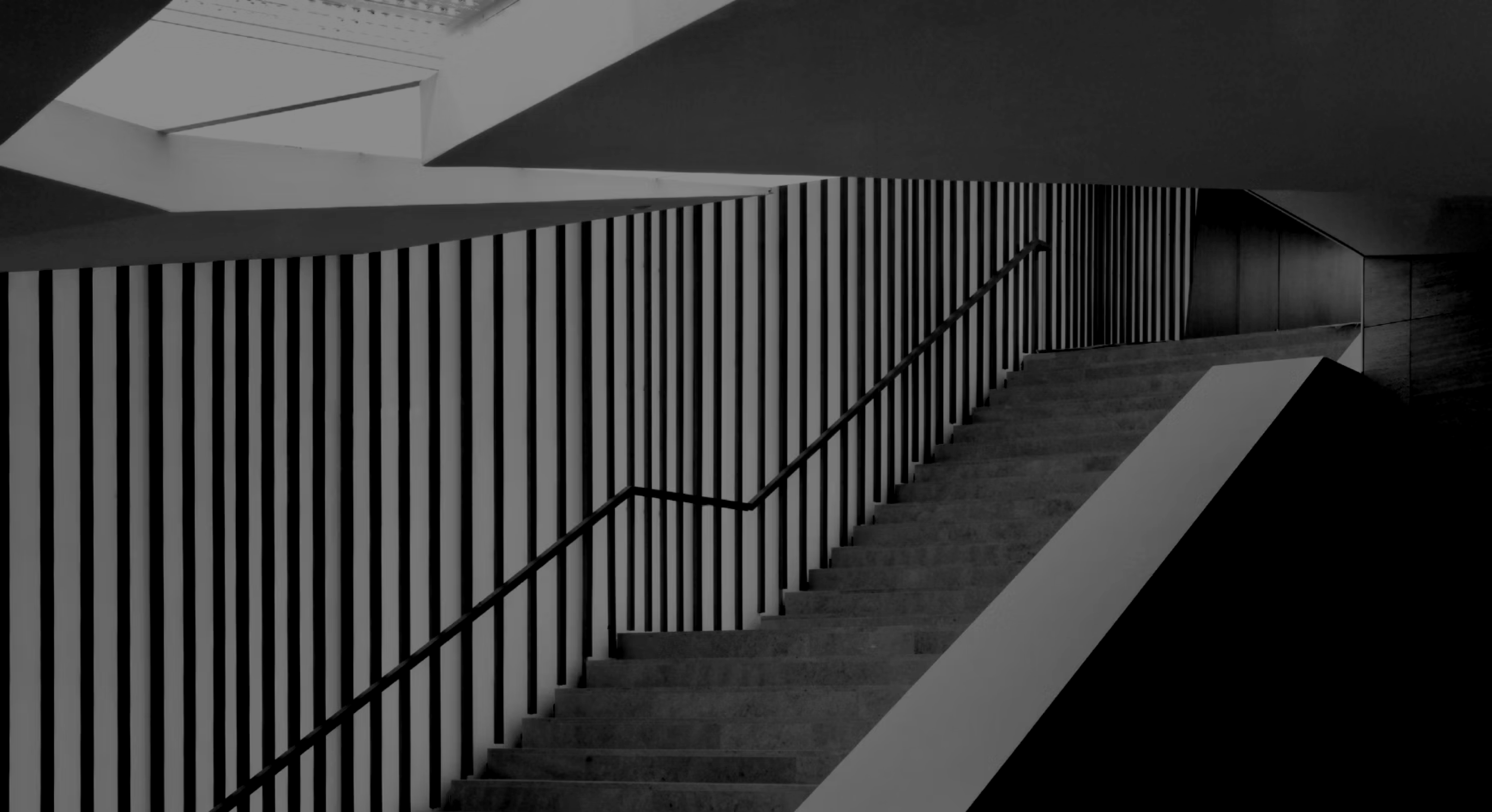 Modern staircase with vertical black bars along the wall and a minimalist handrail in grayscale.
