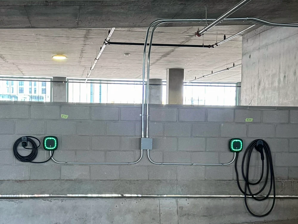 Metal EMT conduit run down a block wall to a junction box, then branching to two wall-mounted EV chargers