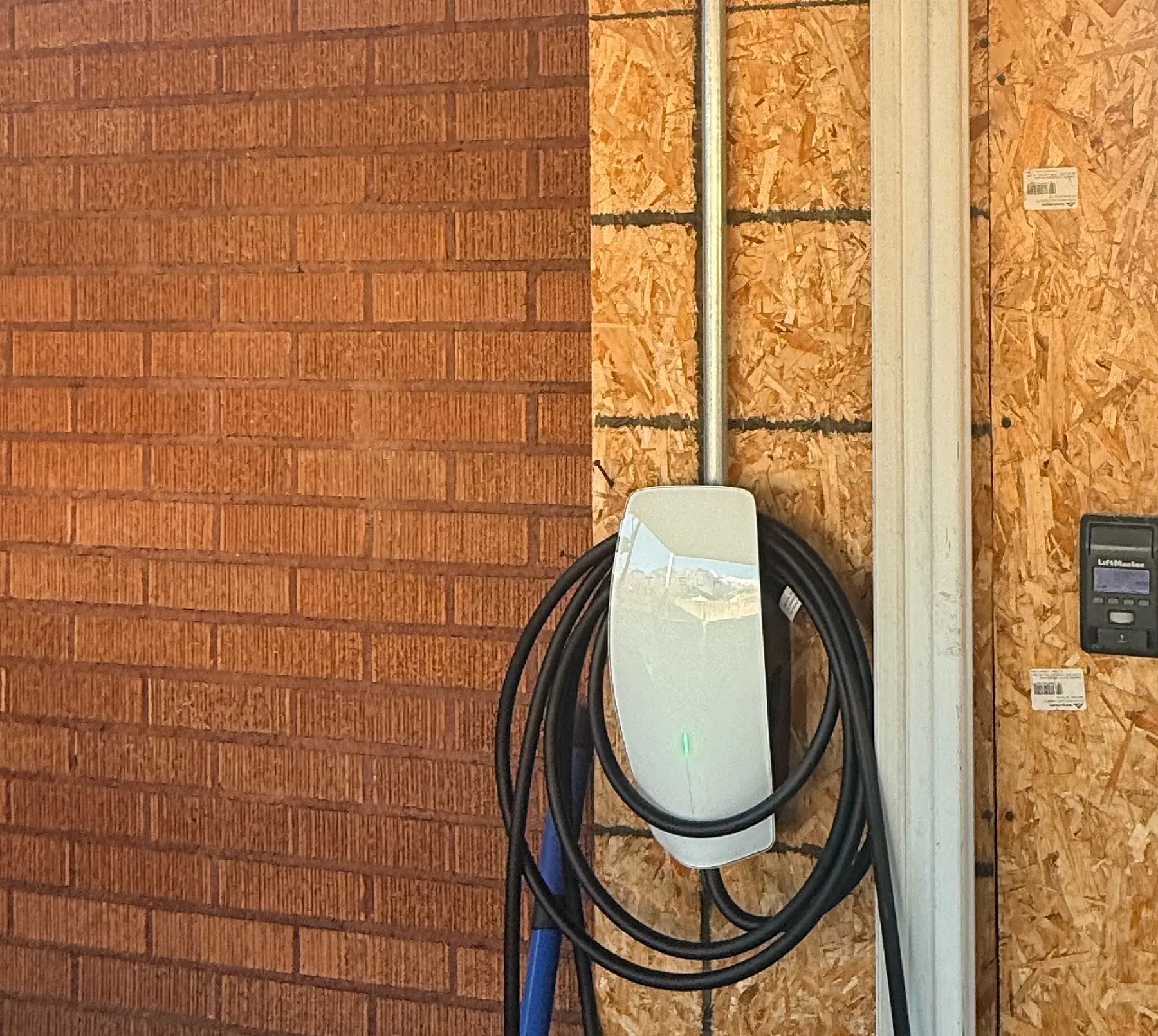 Tesla Wall Connector mounted on an exterior brick wall with conduit run down the trim