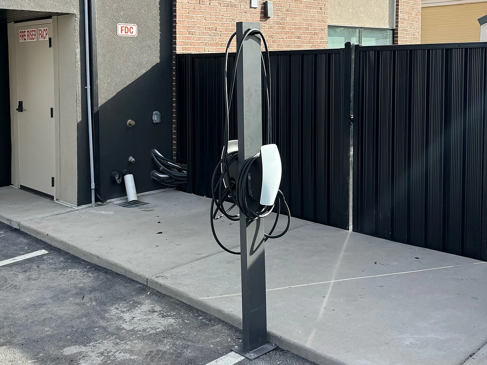 Pedestal-mounted Tesla Wall Connector beside a shared parking area at a multifamily building