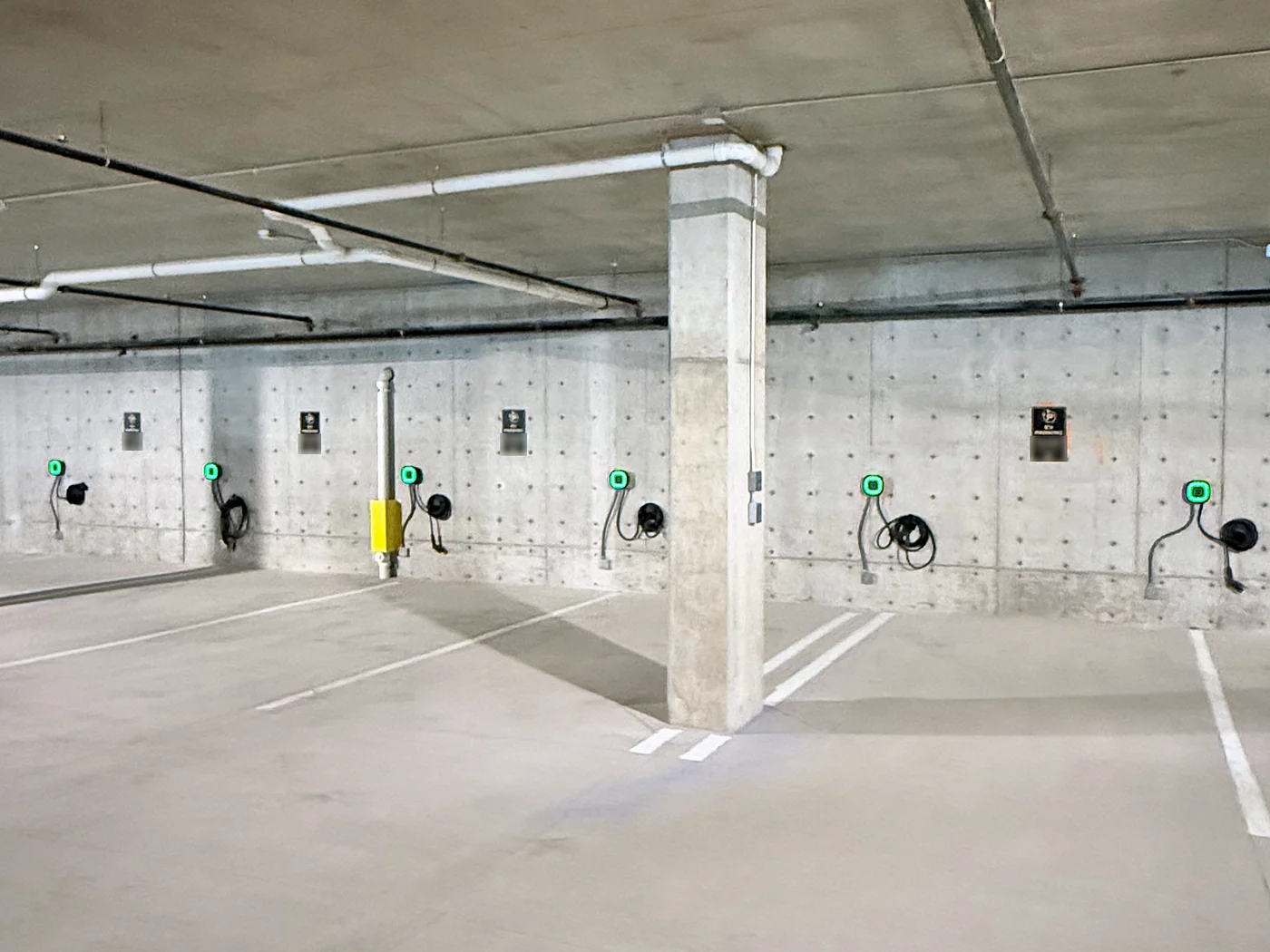 Row of wall-mounted EV chargers with green status lights along the back wall of an underground parking garage