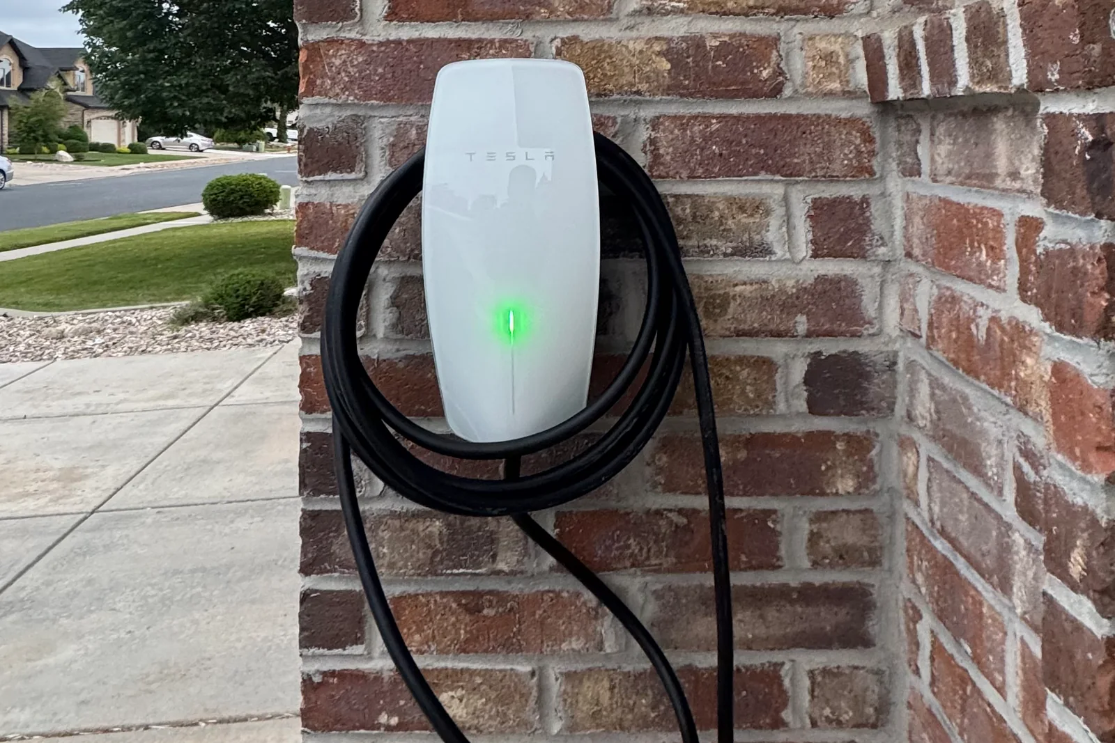 Tesla Wall Connector mounted on an exterior brick wall beside the front entry of a Utah home