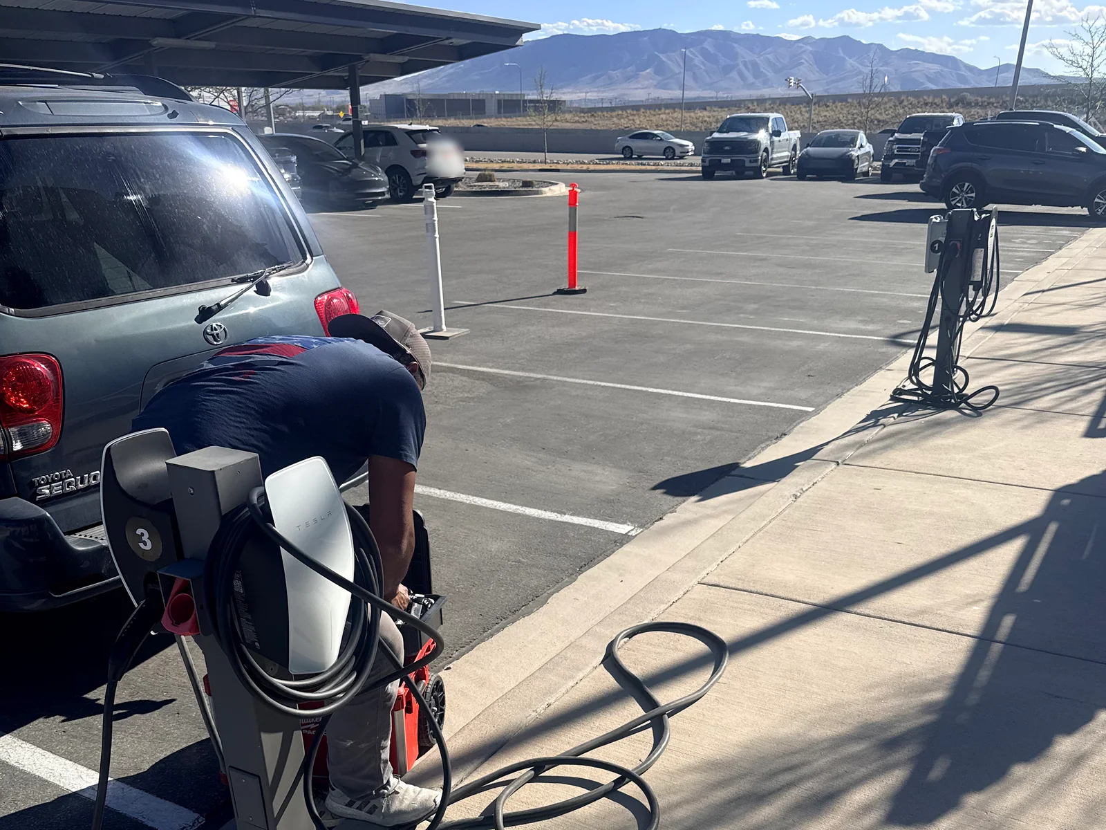 Electrician installing a pedestal EV charger in a covered parking lot with mountains in the background