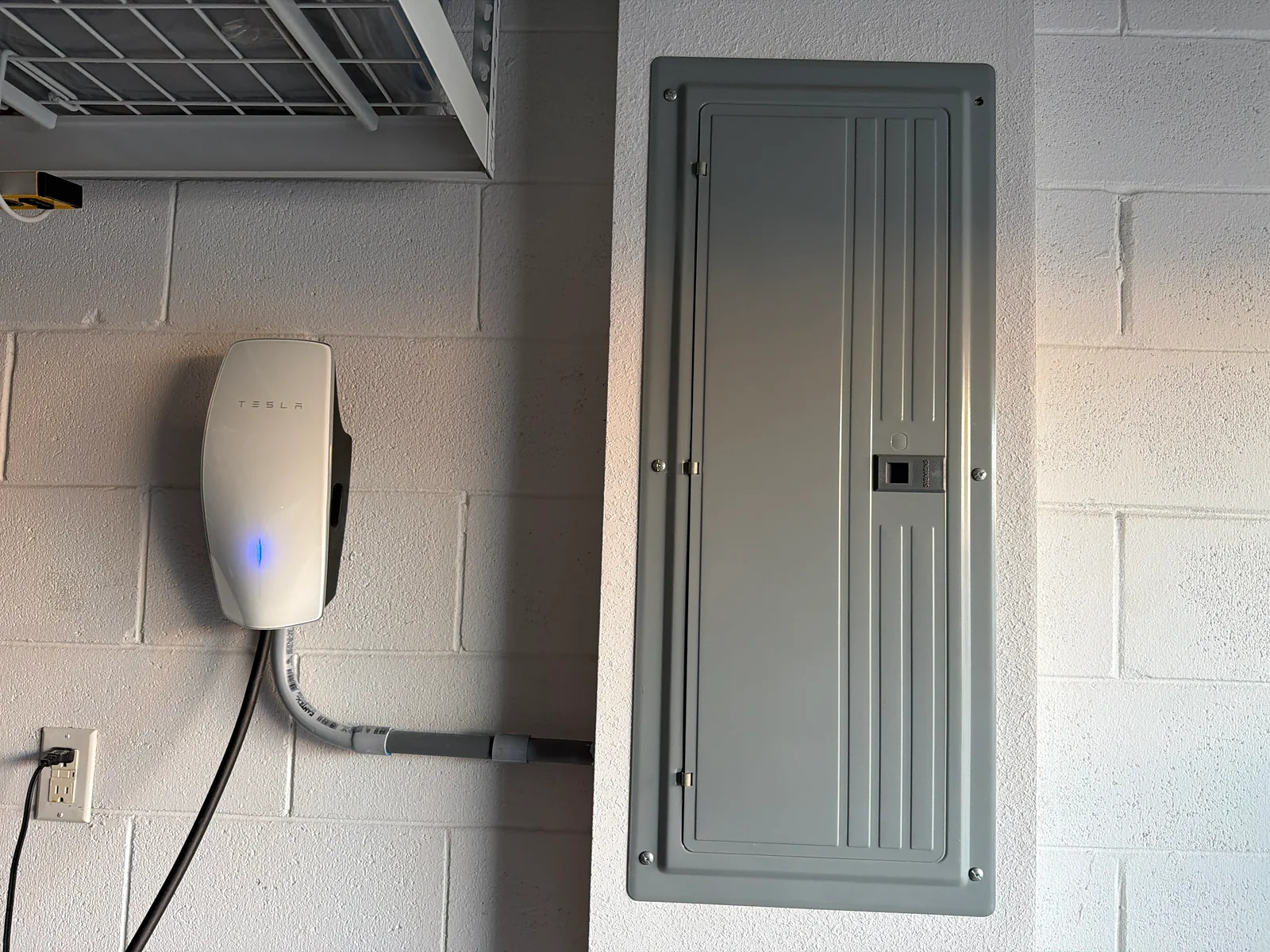 Tesla Wall Connector installed beside a new electrical panel on a painted block garage wall
