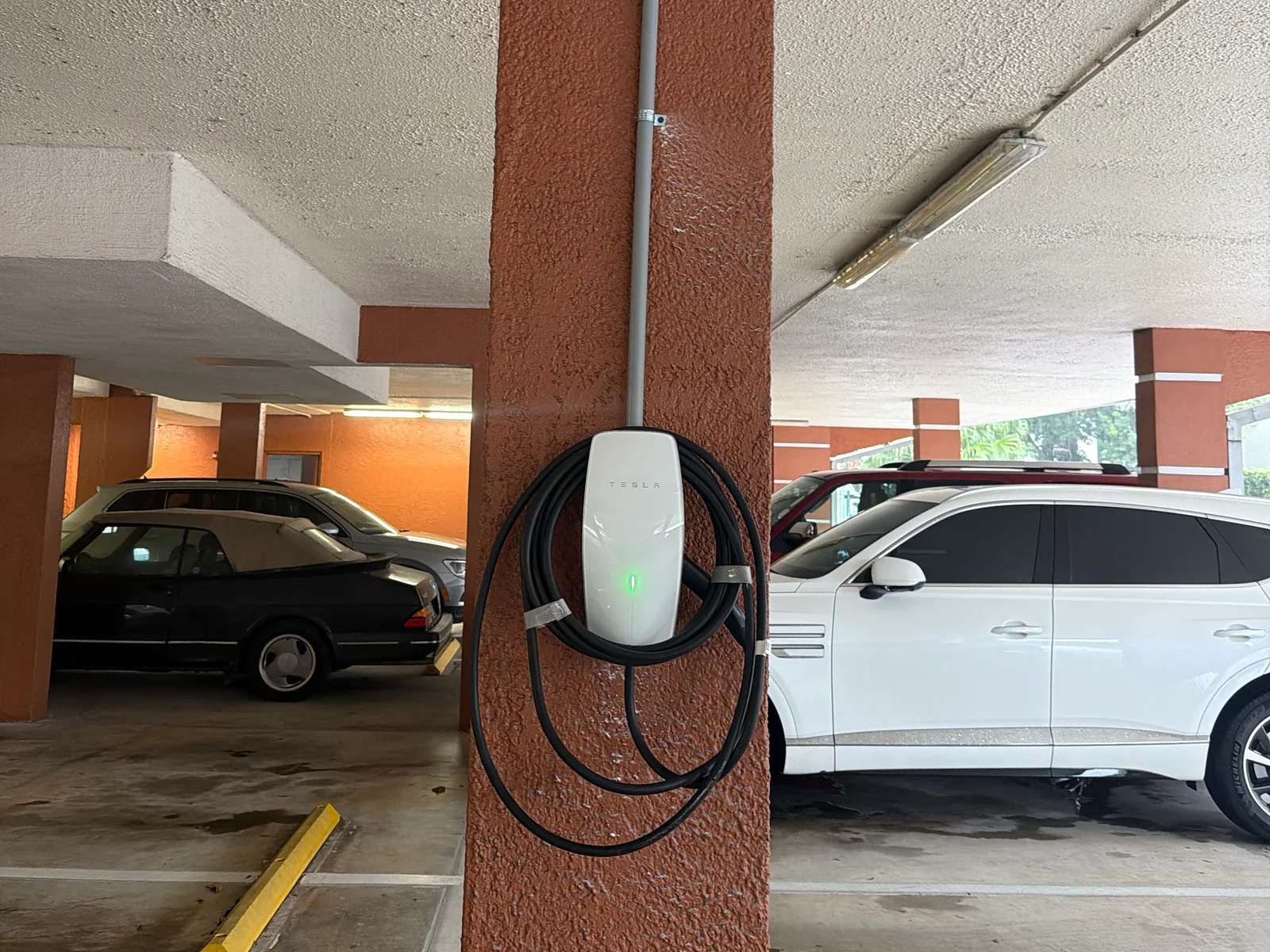 Tesla Wall Connector mounted on a carport column with conduit run along the ceiling of a condo parking area