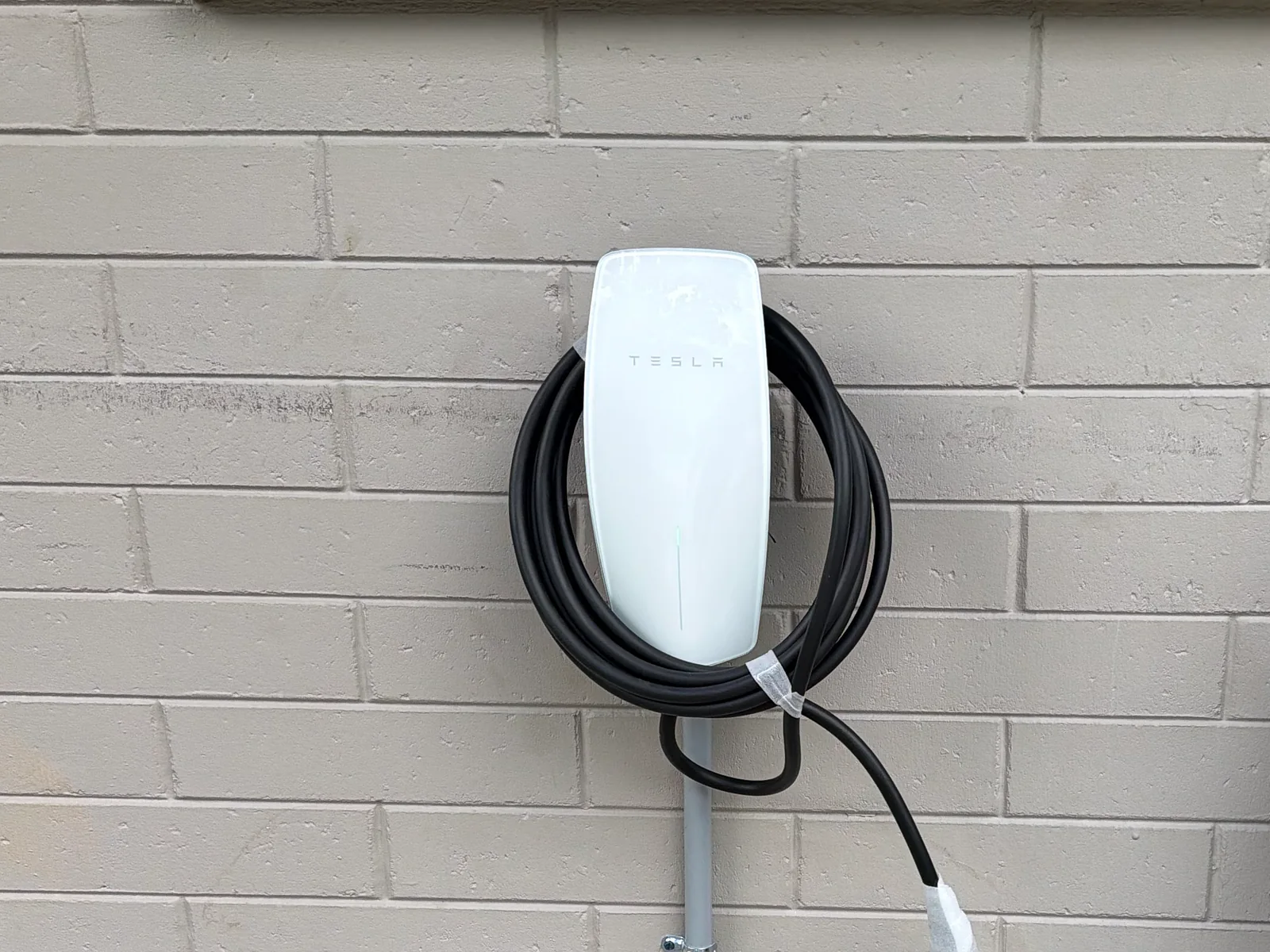 Tesla Wall Connector on an exterior block wall with a short conduit run feeding it from below