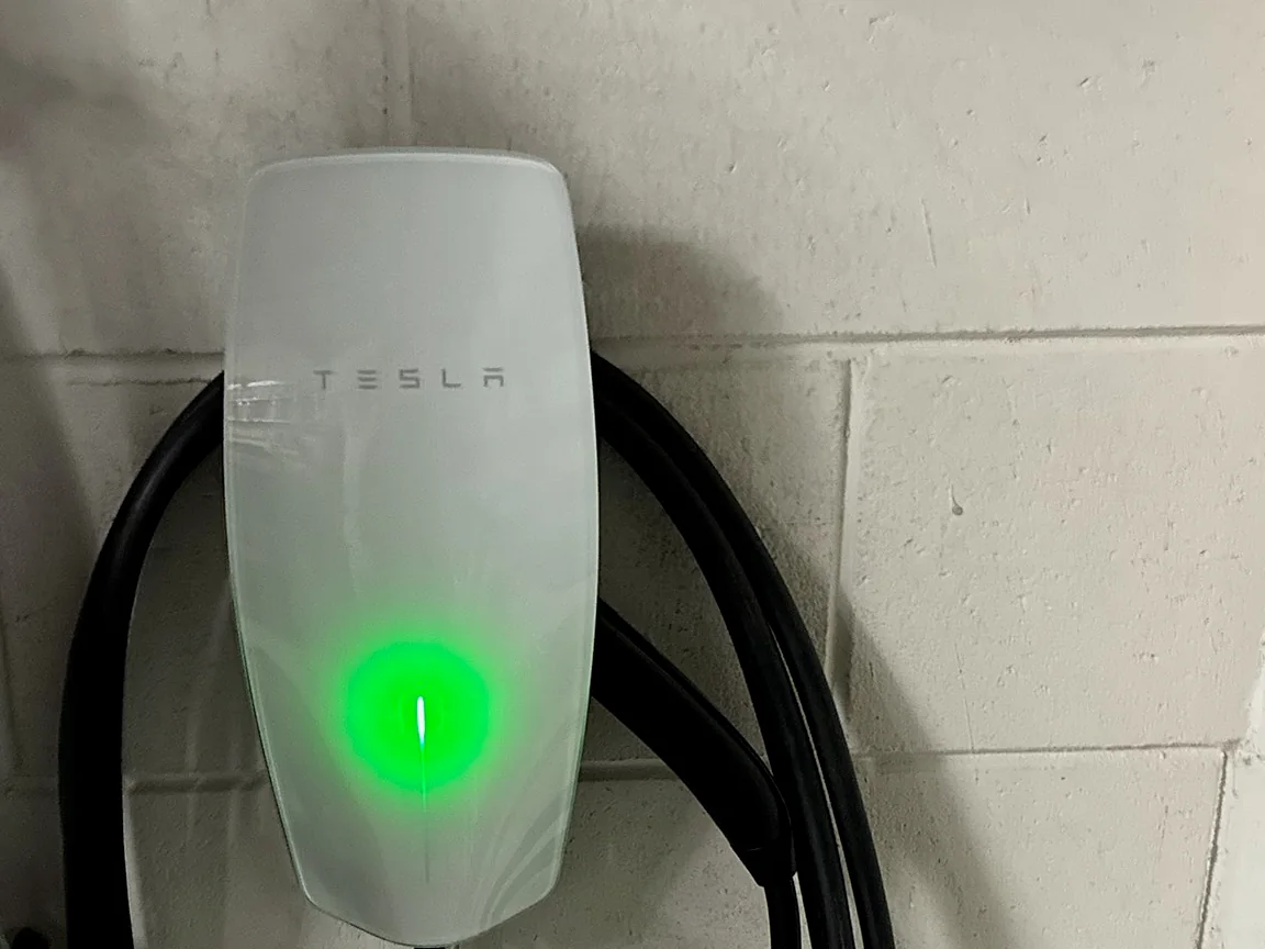 Close-up of a Tesla Wall Connector with its green status light on and the charging cable wrapped neatly