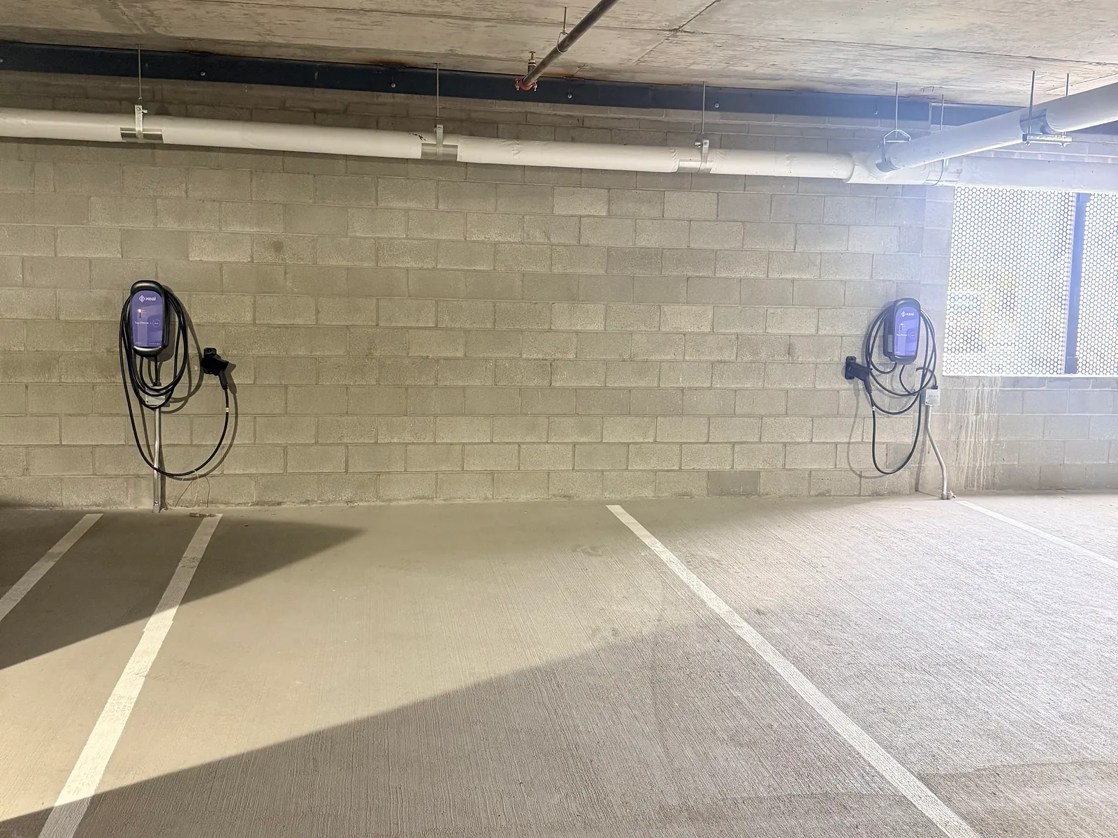 Two wall-mounted Level 2 EV chargers on a block wall in a parking garage