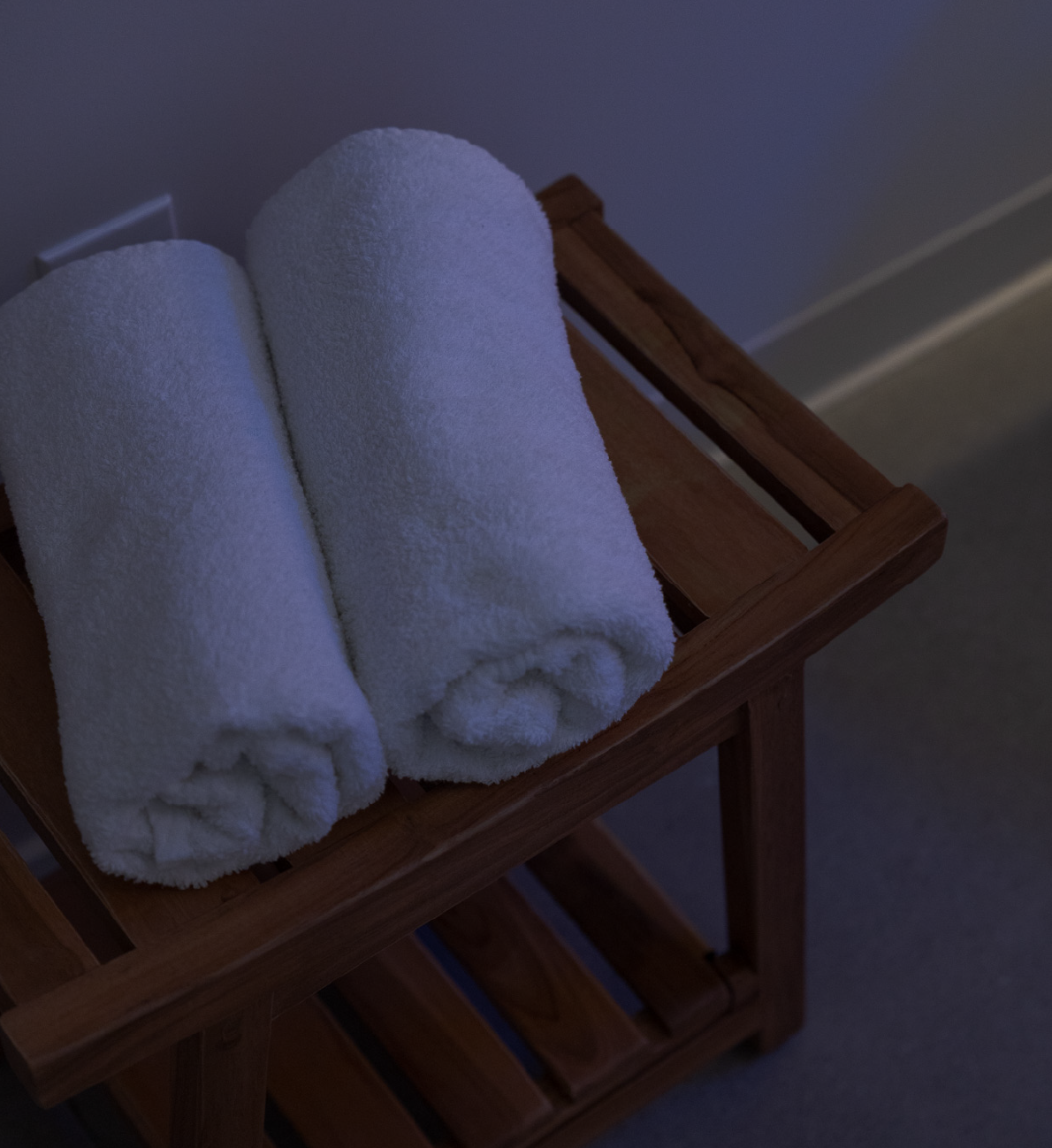 Two white rolled towels placed on a wooden slatted rack.