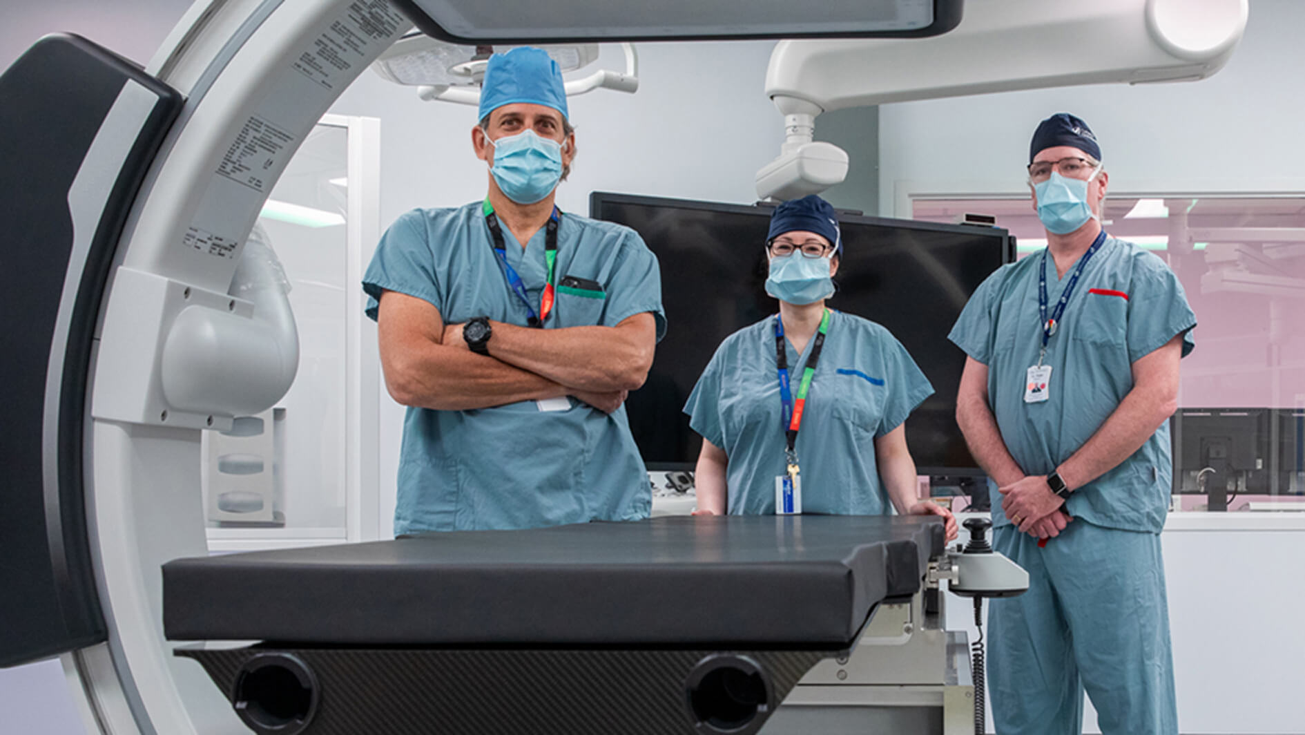 Three surgeons wearing face masks standing in an operating room facing the cameras