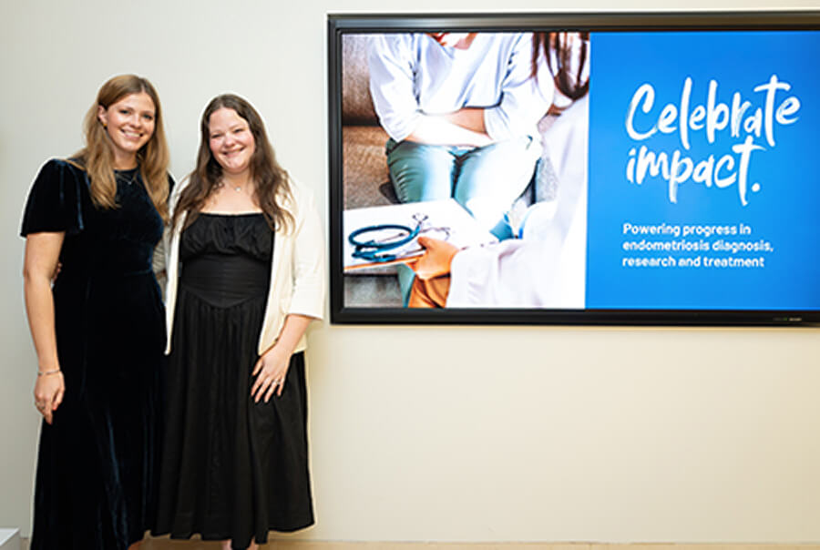 Two women stand beside a screen celebrating new endometriosis chair