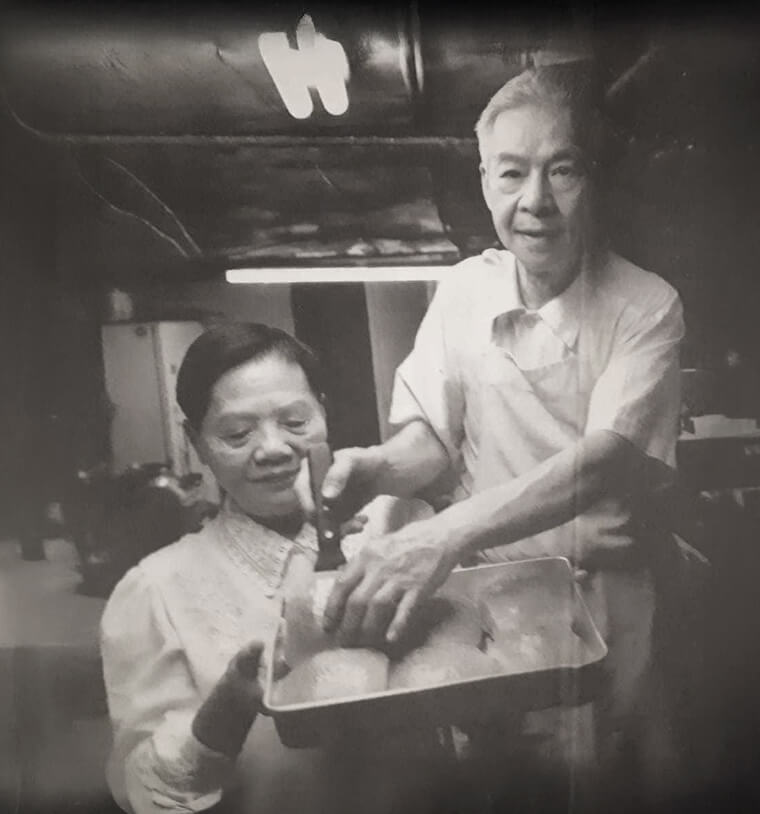 Old black and white photo of man and woman in a basement kitchen holding a tray with baked goods