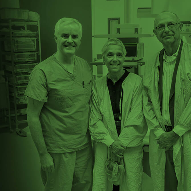 Woman and two men in yellow gowns smiling at the camera in a procedure room