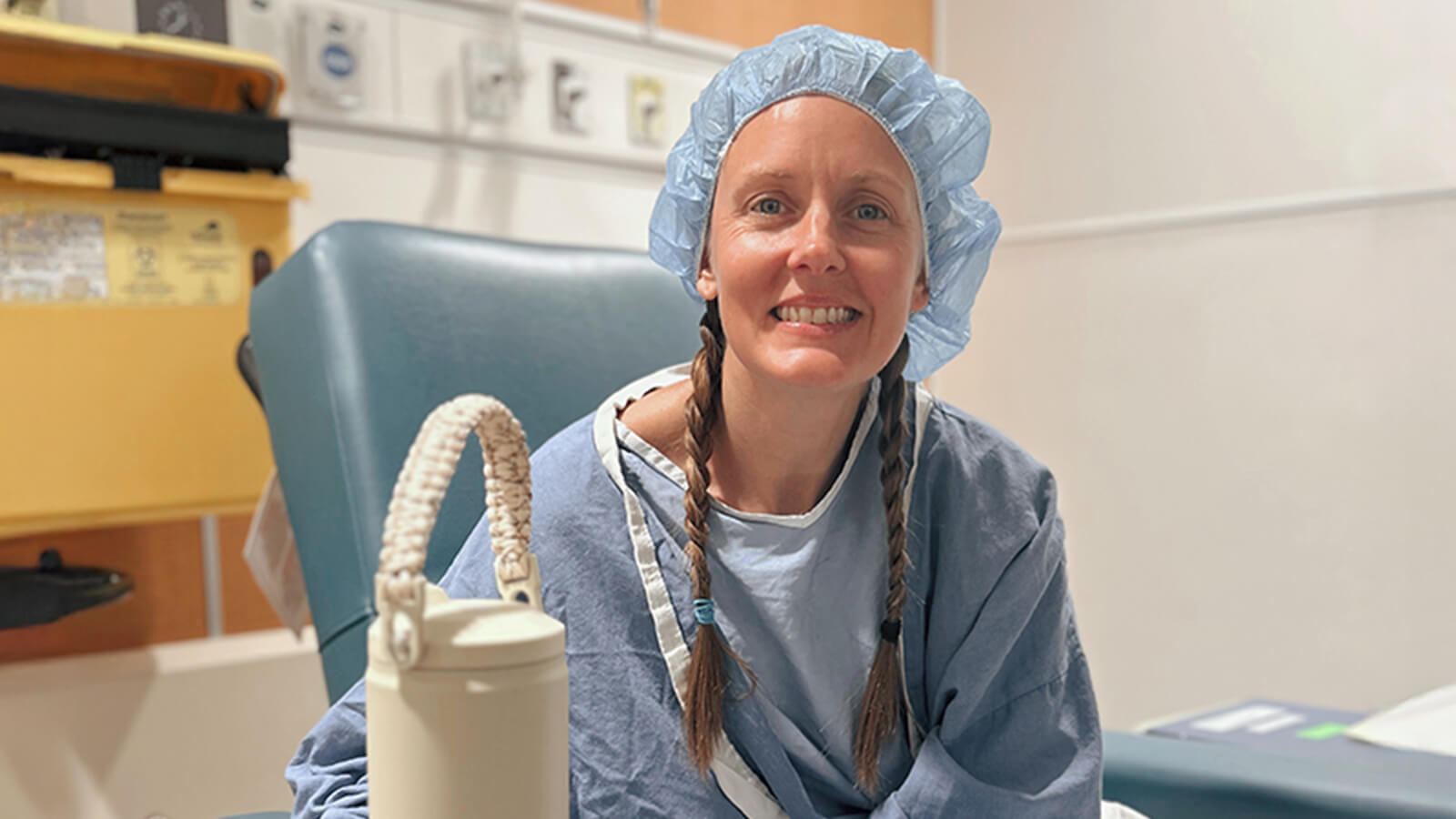 Woman sits in hospital gown and cap, ready for surgery