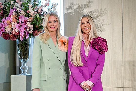 Two stylish women in vibrant mint green and magenta pantsuits posing together