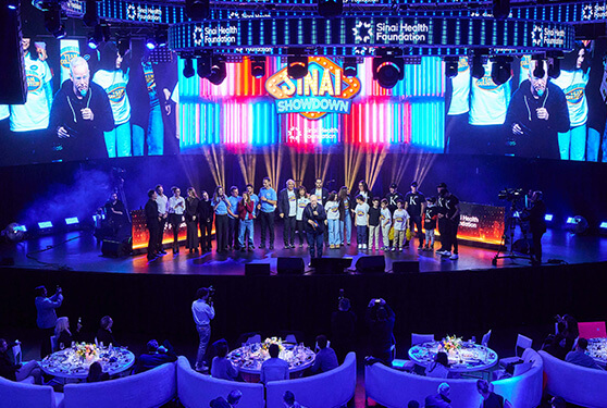 A vibrant event stage with large screens and a seated audience, illuminated by dynamic blue light