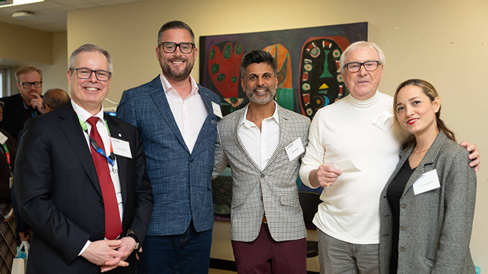 A group of smiling five well dressed individuals posing at a professional gathering