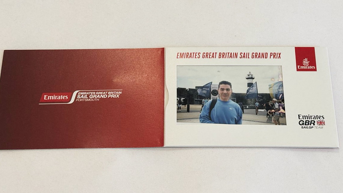 An open folded card branded Emirates Great Britain Sail Grand Prix Portsmouth, holding an instant photograph of the author standing in the fan zone.
