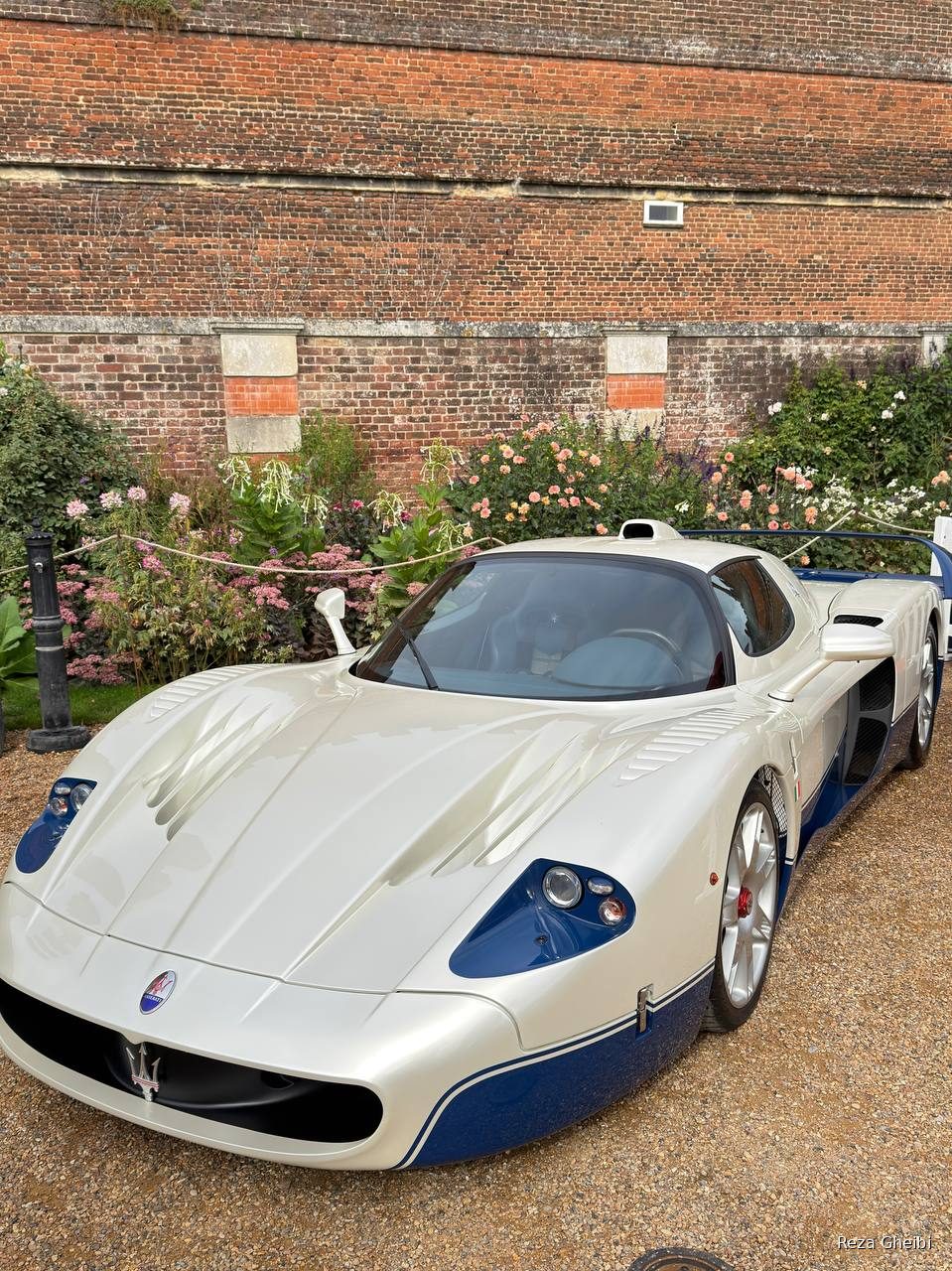 A white and blue Maserati MC12 against the palace brick and flowerbeds.