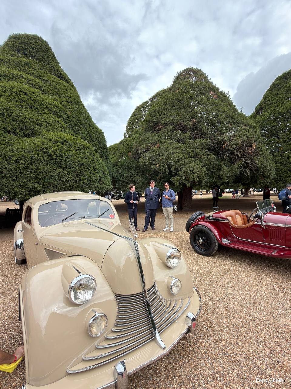 A cream streamlined Art Deco coupe beside a red 1930s Alfa Romeo.