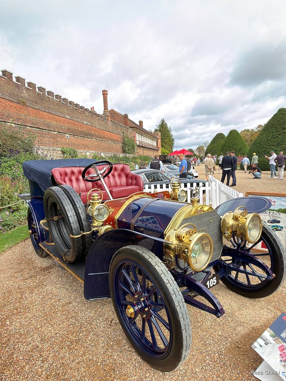 An Edwardian brass-era car in dark blue with brass lamps and buttoned red leather.