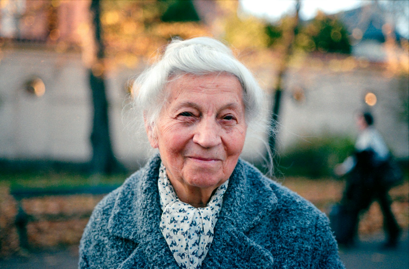 An older woman with white hair and a warm, direct expression, photographed outdoors in autumn light.