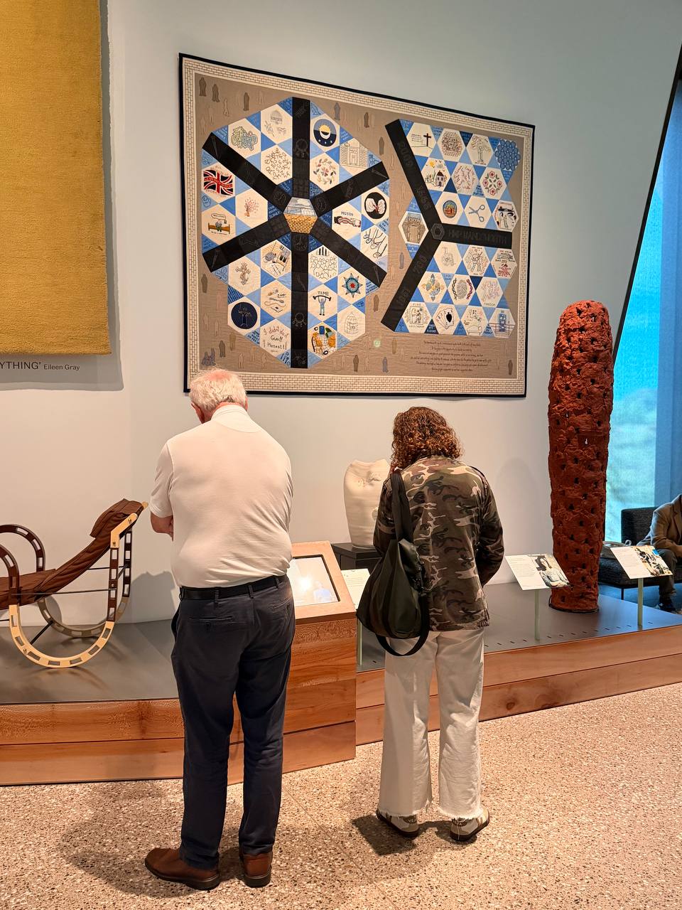 Two visitors read a label beneath a large quilt of hexagonal panels stitched with the words HMP Wandsworth.