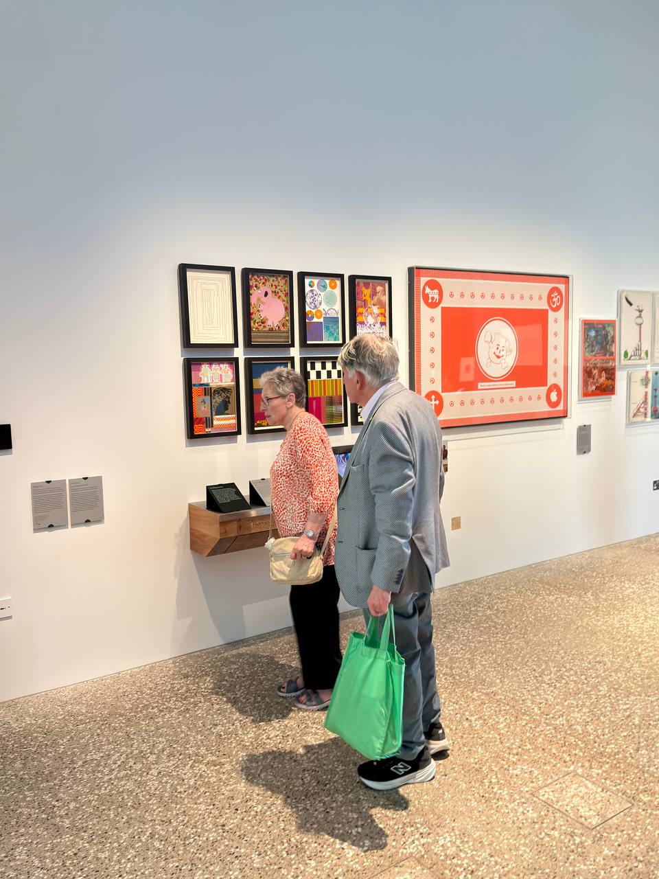 A wide gallery view: children play on the floor while families rest on a long bench beside display cases.
