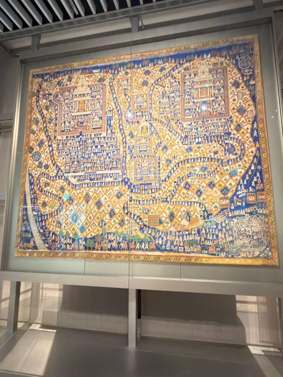A large painted cloth map of Mount Shatrunjaya, dense with temples, pilgrims and winding paths on a blue ground.