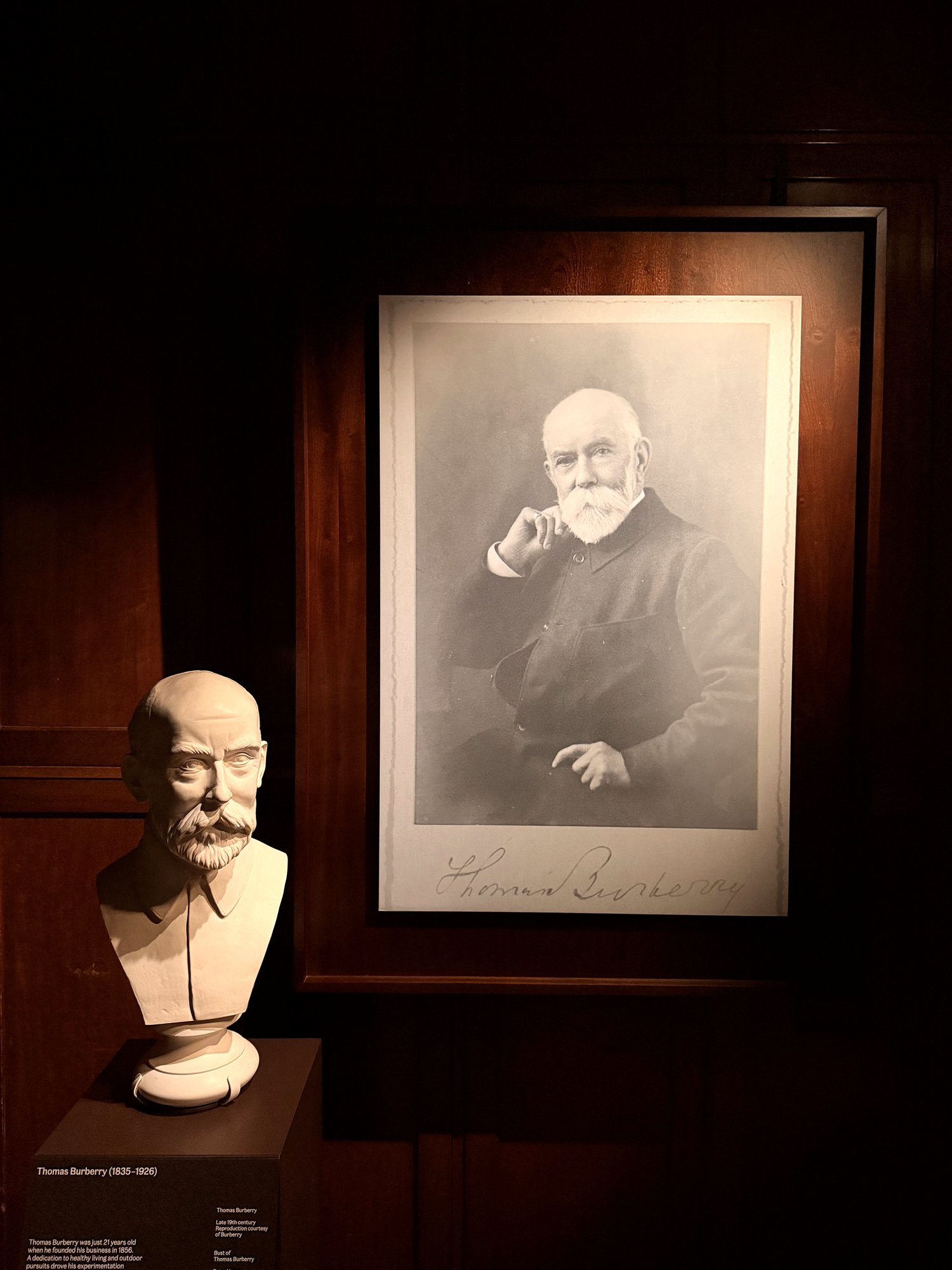 Framed black-and-white photograph of Thomas Burberry beside a white plaster bust, on dark wood panelling.