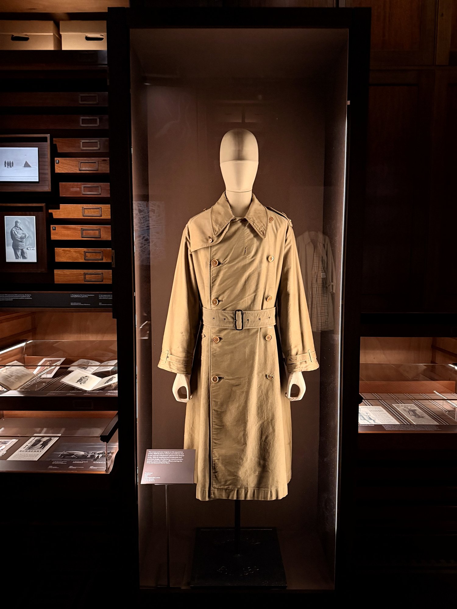 Khaki double-breasted belted trench coat from 1939 on a mannequin in a glass case.