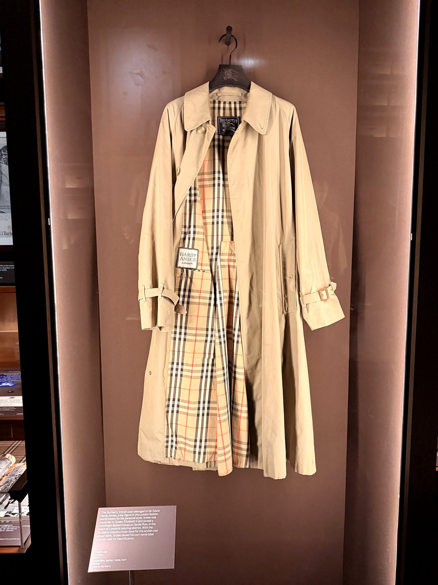 Beige Burberry trench hanging open to show its check lining and a sewn-in label reading Hardy Amies London.