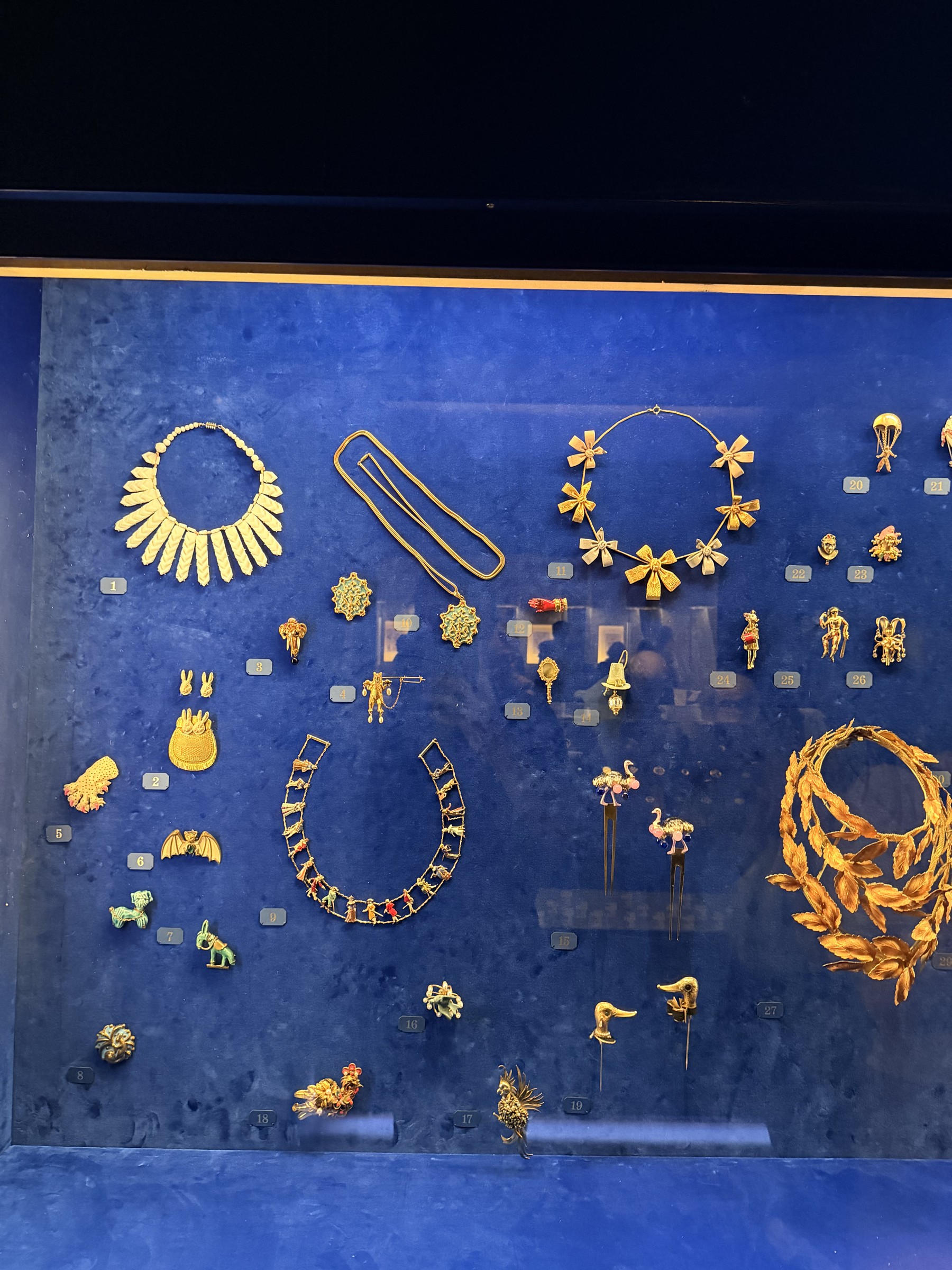 A deep-blue velvet case of gold Schiaparelli novelty jewellery — bows, a laurel wreath, animal and acrobat brooches.