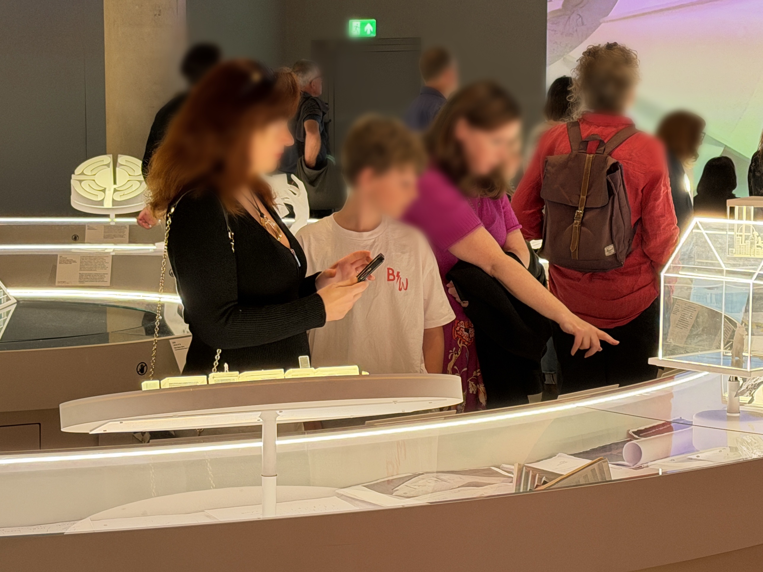 At a model-filled vitrine, an adult points out a work to a teenage boy and a younger child; the faces are blurred for privacy.