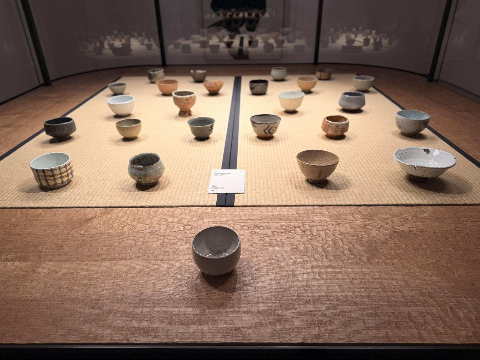 Twenty-five handmade tea bowls arranged on tatami in a vitrine