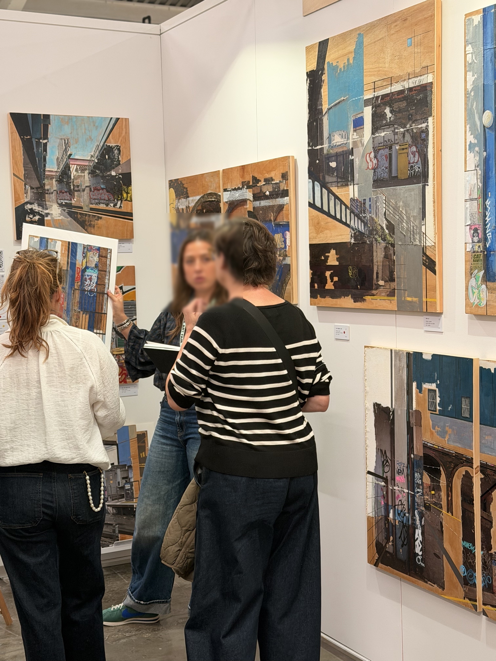 A wall of city scenes built up on wood panels, with visitors moving past