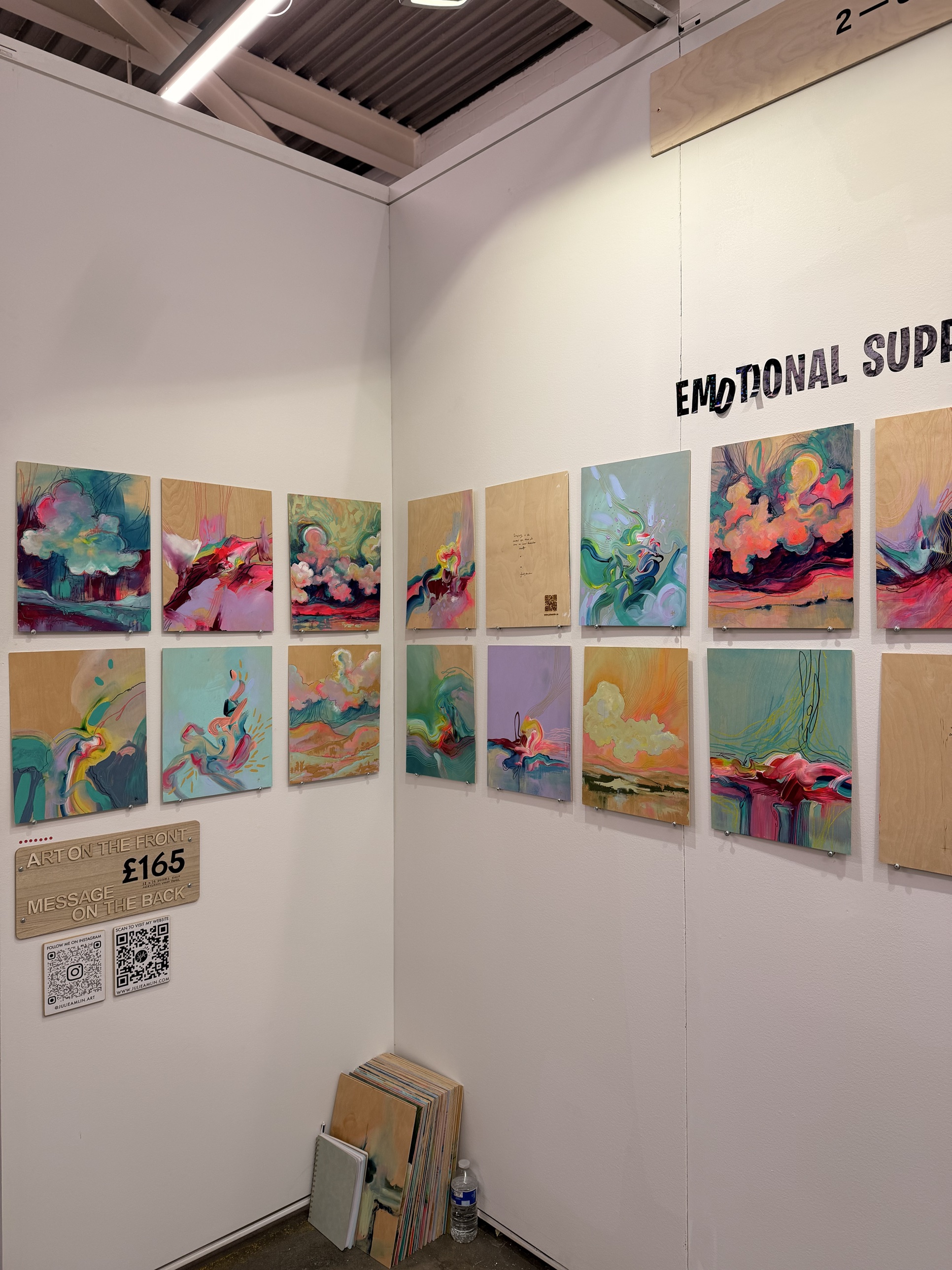 A booth of small cloud paintings on board priced £165, with a sign reading message on the back