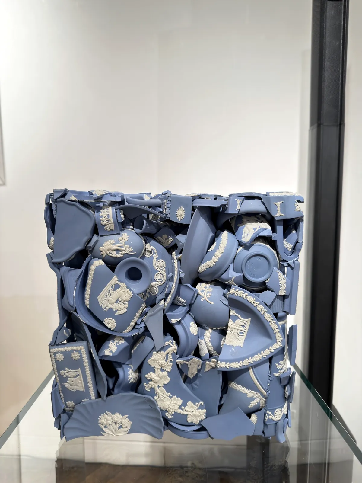 A block of shattered blue and white Wedgwood jasperware fragments compressed into a cube, shown in a glass vitrine